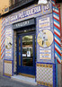 Foto da fachada de uma loja feita de azulejos decorados e que tem anncios. Palavras-chave: Peluquera. Tienda. Comercio. Servicios. Madrid.