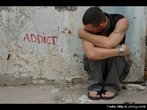 Foto de um rapaz agachado junto ao muro onde se l a palavra "addict" (viciado).  Palavras-chave: drogadito, vcio, drogas, jovem, efeito.
