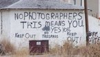 Foto de uma casa aparentemente abandonada, mas com uma inscrio exortando fotgrafos a que mantenham distncia.  Palavras-chave: casa, inscrio, parede, pichao, distncia, funes da linguagem. 