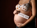 Foto da barriga exposta de uma grvida, que segura um pequeno cartaz com a expresso "Coming soon" (em breve).  Palavras-chave: reproduo, mulher, beb, gravidez, gneros textuais, intertextualidade.