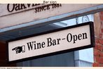 Foto de uma placa indicando um bar que serve vinhos (local no informado).  Palavras-chave: Comrcio. Placa. Ordem frasal. Data.