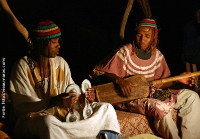 Foto de dois homens negros trajados ao estilo africano, tocando instrumentos típicos.
 Palavras-chave: homem, traje, África, instrumento, música, cultura, interculturalidade, ascendência.