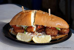 Foto de um sanduíche grande, com pedaços de carne branca e outros ingredientes, sobre um prato.  Palavras-chave: culinária, receita, gênero textual, alimentação. 