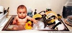  Foto de um bebê sentado em uma pia cheia de água. Ao lado de um patinho de borracha, veem-se também várias panelas e louças sujas. Palavras-chave: mulher, economia, tempo, casa, trabalho, filhos.