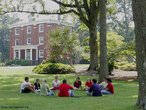 Foto de um grupo de estudantes reunido no gramado de um campus universitário estadunidense tradicional . Ao fundo, vê-se um prédio antigo. Palavras-chave: estudo, companheirismo, ajuda mútua, educação, faculdade. 