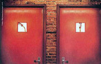 Foto de duas portas de banheiro indicando o sexo fisiológico a que se destina cada uma das salas através da imagem de garrafas.  Palavras-chave: porta, banheiro, garrafa, necessidades, sexo, gênero.