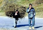  Foto de um homem e uma mulher que vo subindo uma estrada - ele fumando, e ela, carregando um enorme feixe de gravetos.  Palavras-chave: estrada, casal, machismo, interculturalidade, descrio.