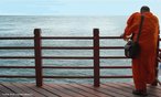 Foto de um monge budista recostado  amurada da praia de Sentosa, em Singapura. O homem permanece de costas para a cmera, que retrata ao fundo o Oceano ndico.  Palavras-chave: religioso, mar, natureza, paisagem, cu, solido, tranquilidade.