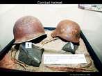 Foto de capacetes usados na Segunda Guerra. O capacete  um dos mais importantes itens do vesturio do soldado, uma vez que se presta a proteger o crebro, rea vital do corpo humano. Palavras-chave: Capacete. Farda. Vesturio. Soldado. Guerra. Crebro. Segurana. Descrio.