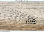 Foto de uma bicicleta parada e desmontada, sobre a areia da praia. Palavras-chave: Bicicleta. Areia. Praia. Diversão. Férias. Relaxamento. Descanso.