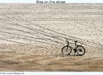 Foto de uma bicicleta parada e desmontada, sobre a areia da praia. Palavras-chave: Bicicleta. Areia. Praia. Diverso. Frias. Relaxamento. Descanso.