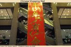 Foto de uma grande faixa escrita em caracteres chineses dourados, disposta próxima à escadaria de uma loja de departamentos em Singapura. Palavras-chave: Ano novo chinês. Interculturalidade. Festejo. Compras.