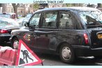 Foto de um "black cab", táxi tradicional de Londres. O automóvel está na rua, entre vários outros, a apresenta uma logomarca da empresa na porta do motorista. Palavras-chave: Transporte. Turismo. Londres. Inglaterra. Tradução. Carro.