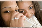 Foto de duas adolescentes bebendo leite em copo de vidro, enquanto olham para a câmera. Palavras-chave: Descrição. Ação. Verbo. To drink. 