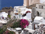 Foto de casas da ilha de Santorini, na Grécia, com predominância do acabamento branco, que reduz o calor devido à forte incidência de sol na região.  Palavras-chave: casa, mar, costa, flores, vegetação.